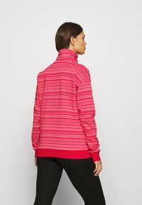 Rød mønstrete genser med høy hals, med geometriske design i hvitt og rosa. Mykt stoff, avslappet passform, ribbestrikkede mansjetter og nederkant.