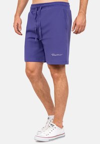 Shorts sportivi viola con vita elastica e cordino. Presentano un ricamo bianco del logo sulla parte inferiore della gamba sinistra. Materiale in misto cotone.