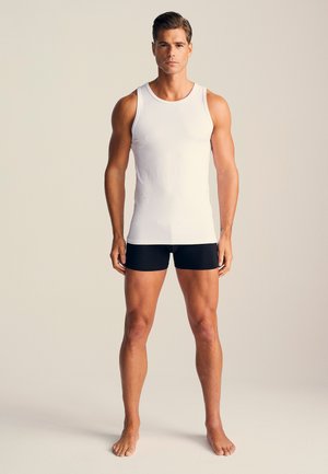Hvid ærmeløs tanktop og sorte boxershorts båret af en mandlig figur. Stoffet ser glat ud med en tætsiddende design.