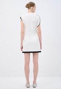 Top bianco a maniche corte con bordi neri, abbinato a una mini gonna bianca con orlo nero. Tessuto morbido; design semplice e moderno.