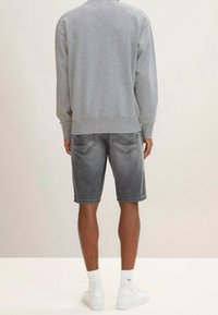 Sudadera gris de corte relajado, combinada con pantalones cortos de mezclilla gris oscuro. Calcetines deportivos blancos y zapatillas completan el conjunto.