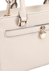 Beige leren handtas met gouden hardware, een gladde textuur en contrasterende stiksels. Bevat een decoratieve bedel en een gestructureerde vorm.