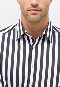 Zwart-witte verticaal gestreepte shirt met een kraag met knoopsluiting, gemaakt van gladde stof en kleine witte knopen langs de knoopsluiting.
