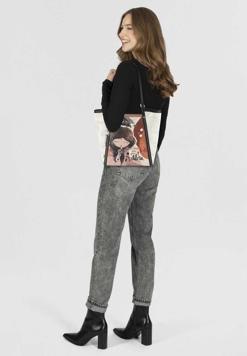 Die Tragetasche hat ein schwarz-weißes Design mit einer bunten Illustration eines Mädchens. Die Tasche kombiniert verschiedene Texturen und hat einen Schultergurt.