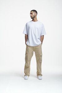 Tricou alb din bumbac cu mâneci scurte, combinat cu pantaloni cargo bej, care au buzunare laterale. Modelul poartă adidași albi.