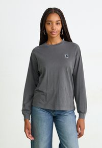 T-shirt en coton gris à manches longues avec un col rond, proposant un petit écusson rectangulaire sur la poitrine gauche et une coupe décontractée.