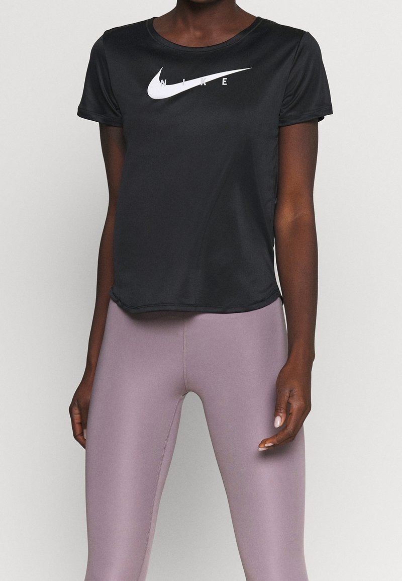 Kvinna iförd en svart kortärmad Nike-topp och högmidjade lavendelfärgade leggings, stående med armarna avslappnat längs sidorna.