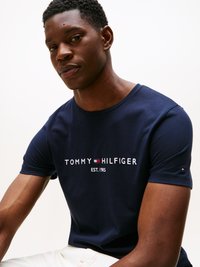 Mørkeblå bomulds T-shirt med "TOMMY HILFIGER" logo i hvid, rød og blå, samt et lille logo på ærmet. Korte ærmer, rund hals.