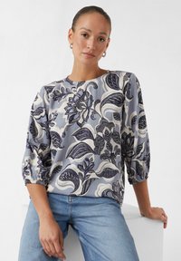 Bluse mit floralem Druck, die einen blau-grauen Hintergrund, Dreiviertelärmel mit elastischen Bündchen und detaillierte marineblaue und weiße Muster aufweist.