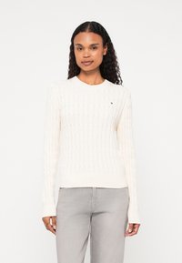 Kremowy sweter w splot warkoczowy z okrągłym dekoltem, prążkowanym dołem i długimi rękawami; posiada małe logo na piersi.