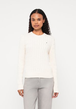 Kermainen kabelineulepullover pyöreällä pääntiellä, ribbaushelmalla ja pitkillä hihoilla; jossa on pieni logo rinnassa.