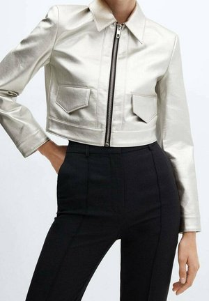Gekürzte metallisch silberne Jacke mit Frontreißverschluss und Klappentaschen, kombiniert mit hoch taillierter schwarzer Hose bei einer stehenden Person.