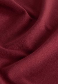 Material moale și neted, de culoare roșu închis, cu pliuri fine și textură fină de tricot vizibilă.