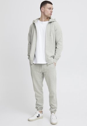 Light gray hoodie with front zipper and drawstrings, paired with matching sweatpants. White t-shirt underneath and white sneakers.