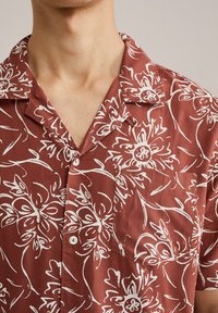 Chemise à manches courtes, bourgogne, avec un motif floral blanc et une poche, fabriquée dans un tissu doux avec un col et une fermeture à boutons.
