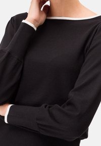 Schwarzer Pullover mit Bootsausschnitt, langen puffigen Ärmeln und weißem Besatz entlang des Halsausschnitts und der Ärmelbündchen, hergestellt aus weichem Strickmaterial.