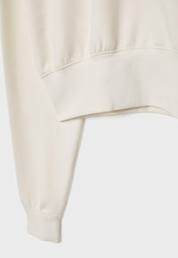 Felpa color crema con tessuto testurizzato, polsini a coste e orlo leggermente curvato per una vestibilità rilassata.