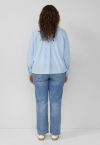 Lichtblauw en wit gestreept shirt met lange mouwen, gecombineerd met lichtblauwe jeans en witte sneakers. Zachte textuur, comfortabele pasvorm.