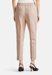 Lichtroze gestreepte broek met een elastische tailleband, taps toelopende pijpen en opgerolde manchetten. Aan de achterkant bevinden zich twee zakken. Gecombineerd met zwarte hakken.