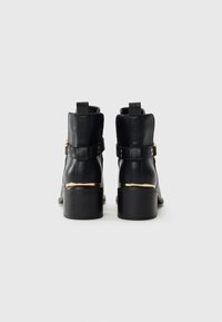 Black leather ankle boots with a smooth finish, featuring a gold accent band and textured black heel. No visible branding.