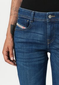 Jeans en denim bleu marine avec une coupe classique, ornés de coutures orange, d'un bouton argenté et d'un tag logo sur la poche avant.