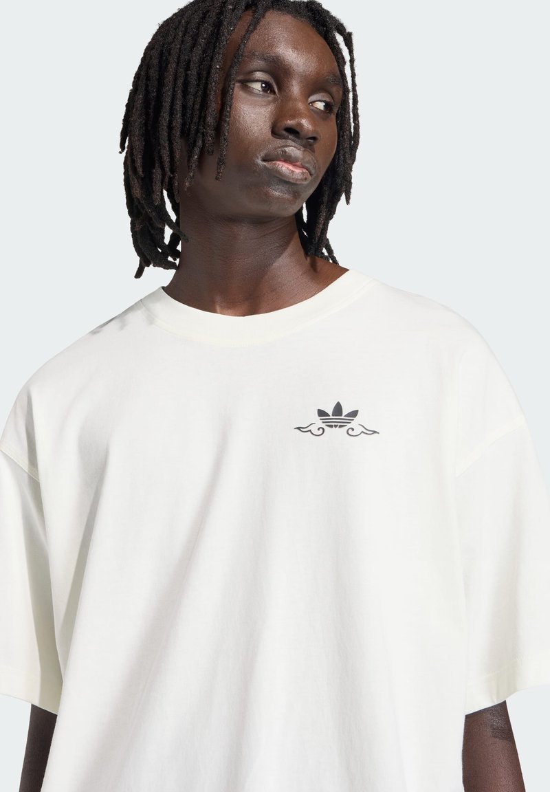 T-shirt en coton blanc à coupe ample, avec un petit logo Adidas noir orné d'accents ondulés sur la poitrine. Texture douce.