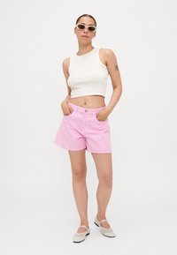 Pantalones cortos a rayas rosas con un corte relajado, cierre de botón en la parte delantera y dos bolsillos laterales, combinados con una blusa blanca ajustada sin mangas y unas gafas de sol.