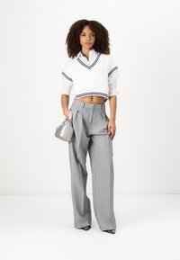 Pulover alb scurt cu dungi navy, asociat cu pantaloni gri plisati, cu talie inalta. Modelul tine o geanta mica argintie si poarta pantofi negri ascutiti.