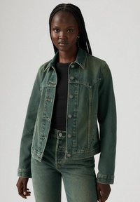 Denim jacket in a dark green wash with a classic cut, button closures, and two chest pockets; paired with matching green jeans.