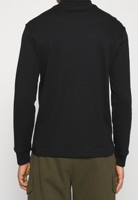 Svart långärmad tröja med hög krage, gjord av mjukt tyg. Har minimala sömmar och en avslappnad passform. Synliga ribbade ärmslut.