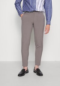 Ljust bruna skräddarsydda byxor med smal passform, mjuk textur och subtil veckdetalj, tillsammans med svarta loafers och en skjorta med blå ränder.