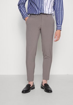 Pantalones de traje en color marrón claro con un ajuste Slim, textura suave y un sutil detalle de pliegue, combinados con mocasines negros y una camisa a rayas azul.