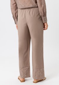 Pantalons à jambes larges beige clair avec une finition texturée. Caractéristiques des accents brodés au bas et une taille élastique pour le confort.