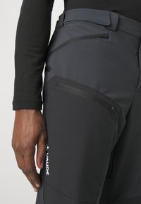 Zwarte outdoorbroek van synthetisch materiaal, met zijzakken met ritsen, een slim fit en een logo op de bovenbenen.
