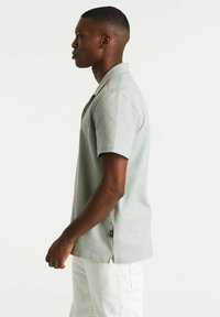 Polo à rayures à manches courtes en vert clair et blanc. Doté d'un col classique, d'échancrures sur les côtés et d'une petite étiquette logo à l'ourlet.