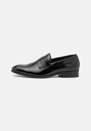 Pantofii loafer din piele neagră au o finisare netedă și lucioasă, cu un model texturat subtil pe partea superioară. Tocul este jos și robust, iar forma vârfului este rotunjită.