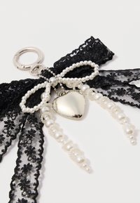 Schwarzes Spitzenband mit weißen Kunstperlen und einem silbernen Herzanhänger, mit filigranen Details und geschichteten Texturen. Schlüsselringbefestigung inklusive.