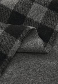 Woolen fabric with a black and gray checkered pattern, featuring a soft, textured surface and a folded edge revealing a gray underside.