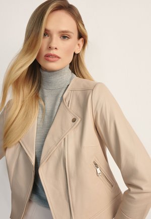 Jasnobeżowa skórzana kurtka z ukośnym zamkiem błyskawicznym, kołnierzem na zatrzask i boczną kieszenią; nałożona na szary sweter z golfem.