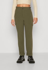 Pantaloni cargo verde oliva con vita alta, chiusura con bottone, tasche laterali, vestibilità affusolata e orli leggermente risvoltati. Indossati con sneakers nere.