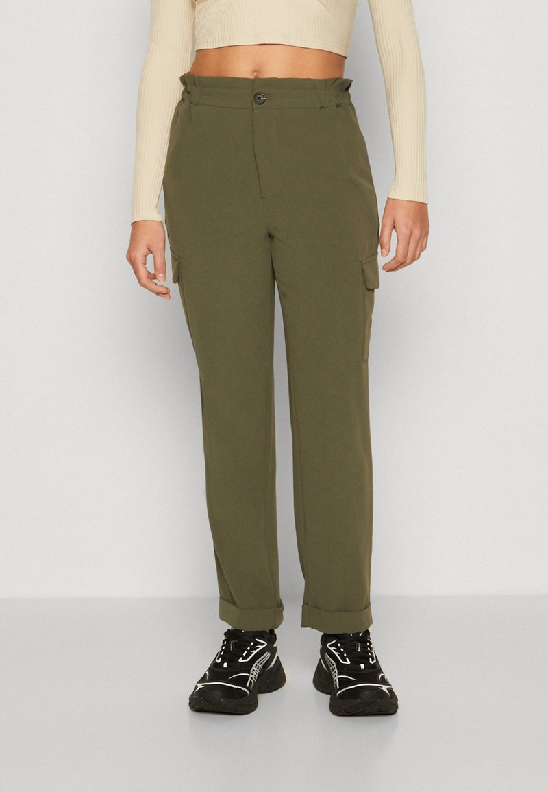 Pantaloni cargo verde oliva con vita alta, chiusura con bottone, tasche laterali, vestibilità affusolata e orli leggermente risvoltati. Indossati con sneakers nere.