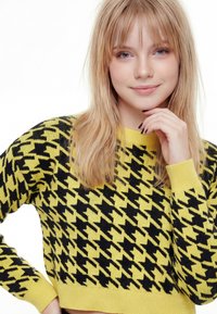 Pletený sveter v žiarivej žltej farbe s čiernym vzorom psa na štvorčekoch. Má rebrované manžety a výstrih, skrátený strih. Mäkká textúra.