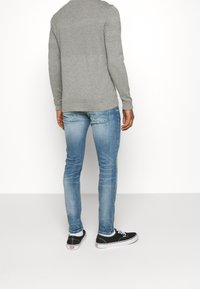 Šedý svetr s texturovanými zády v kombinaci s světle modrými úzkými džínami a černými teniskami. Oblečení představuje neformální vzhled.