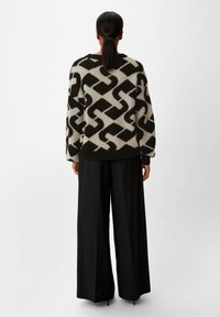 Geprinte gebreide trui in zwart en crème kleuren. Beschikt over een geometrisch ontwerp met een relaxte fit en geribbelde manchetten en zoom. Gepaard met zwarte wijde broek.