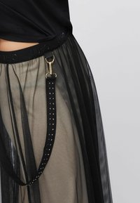 Gonna nera trasparente con vita a fascia solida, dotata di una cinghia nera staccabile con borchie argento e clip dorata.