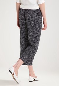 Czarno-białe wzorzyste spodnie 3/4 z lekkiego materiału, z elastycznym pasem i luźnym krojem, zestawione z białymi płaskimi butami.