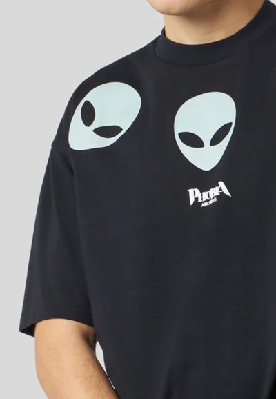 T-shirt in cotone nero con due grafiche di teste di alieno azzurro chiaro sul davanti e un testo logo bianco vicino al centro in basso.