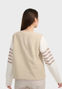 Gilet in pile beige con maniche lunghe bianche e righe marroni. Tessuto morbido, collo tondo e vestibilità comoda.