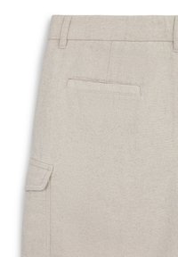 Pantalons en tissu texturé beige avec une poche arrière plate et une poche cargo sur le côté, présentant une coupe ajustée et des lignes épurées.