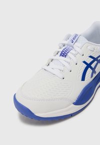 White athletic shoe with blue accents, textured mesh upper, smooth synthetic overlays, and a cushioned sole. Laces and branded tag are visible.